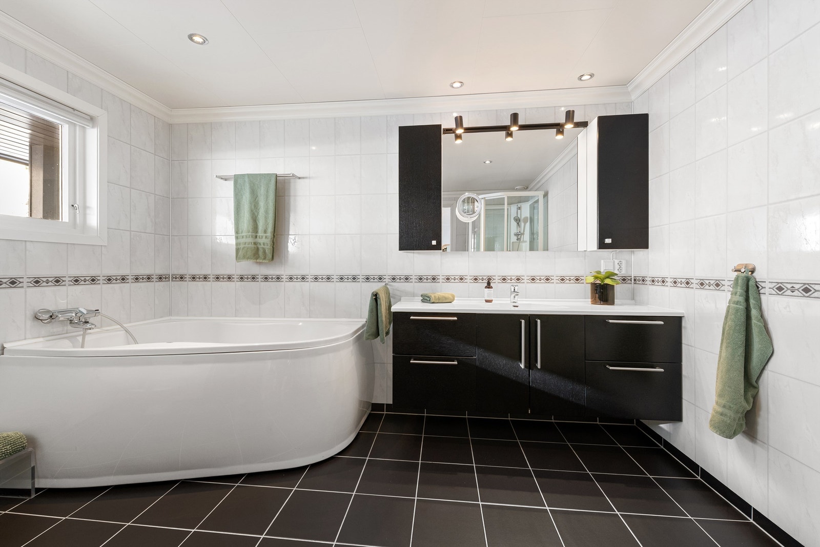 Romslig innredning med sorte glatte fronter og ovenpåliggende servant. Speil med overlys og skap over servant. Galleribilde