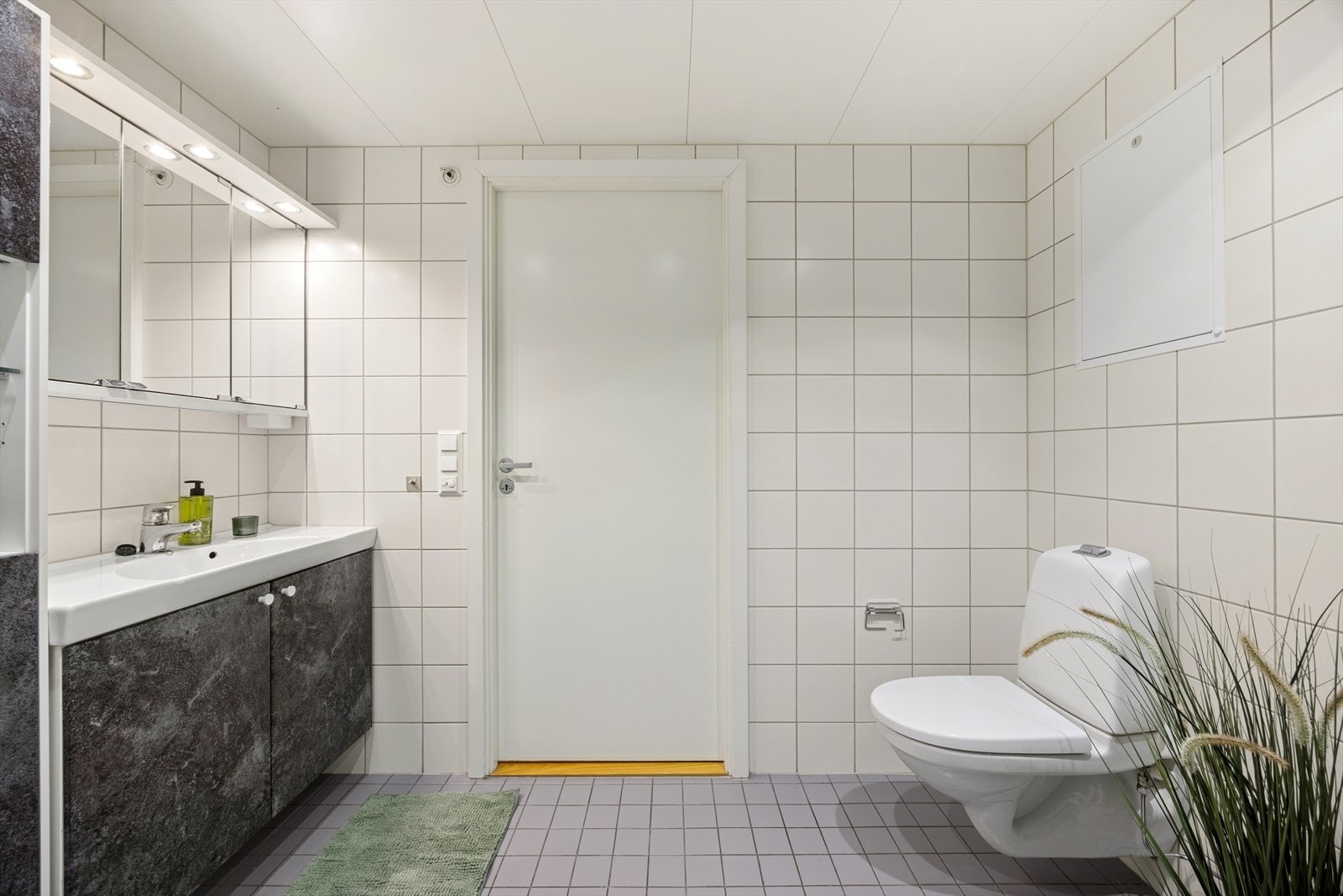 Badet er innredet med servantskap med ett-greps blandebatteri, speilskap, vegghengt toalett, avskjermet dusjhjørne med glass, blandebatteri og dusjgarnityr. Galleribilde