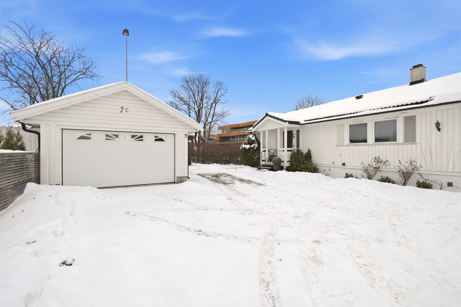 Garasje på gårdsplass med elektrisk styrt port og ytterligere parkeringsmuligheter på tomt. El-billader plassert på utsiden av garasje. Sensorstyrte spotter og lys ved garasje. Galleribilde