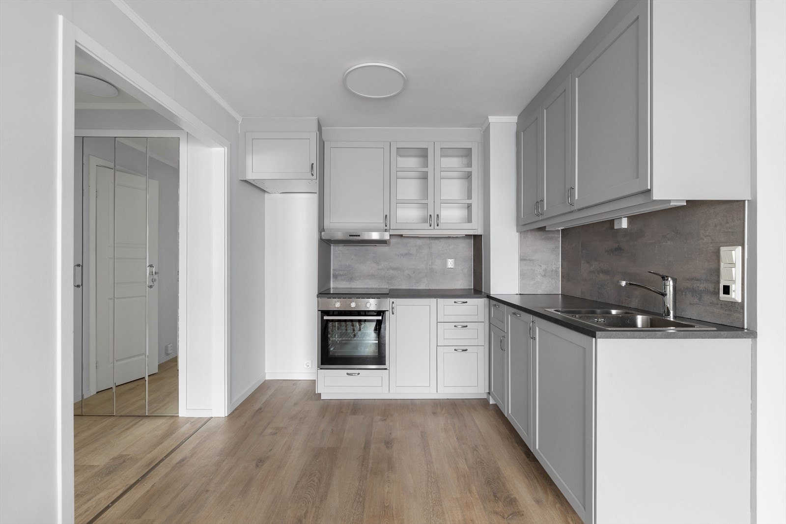 Pent kjøkken med profilerte fronter i grå og benkeplate av laminat. På veggen over benken er det våtromsplater, for enkel rengjøring Galleribilde