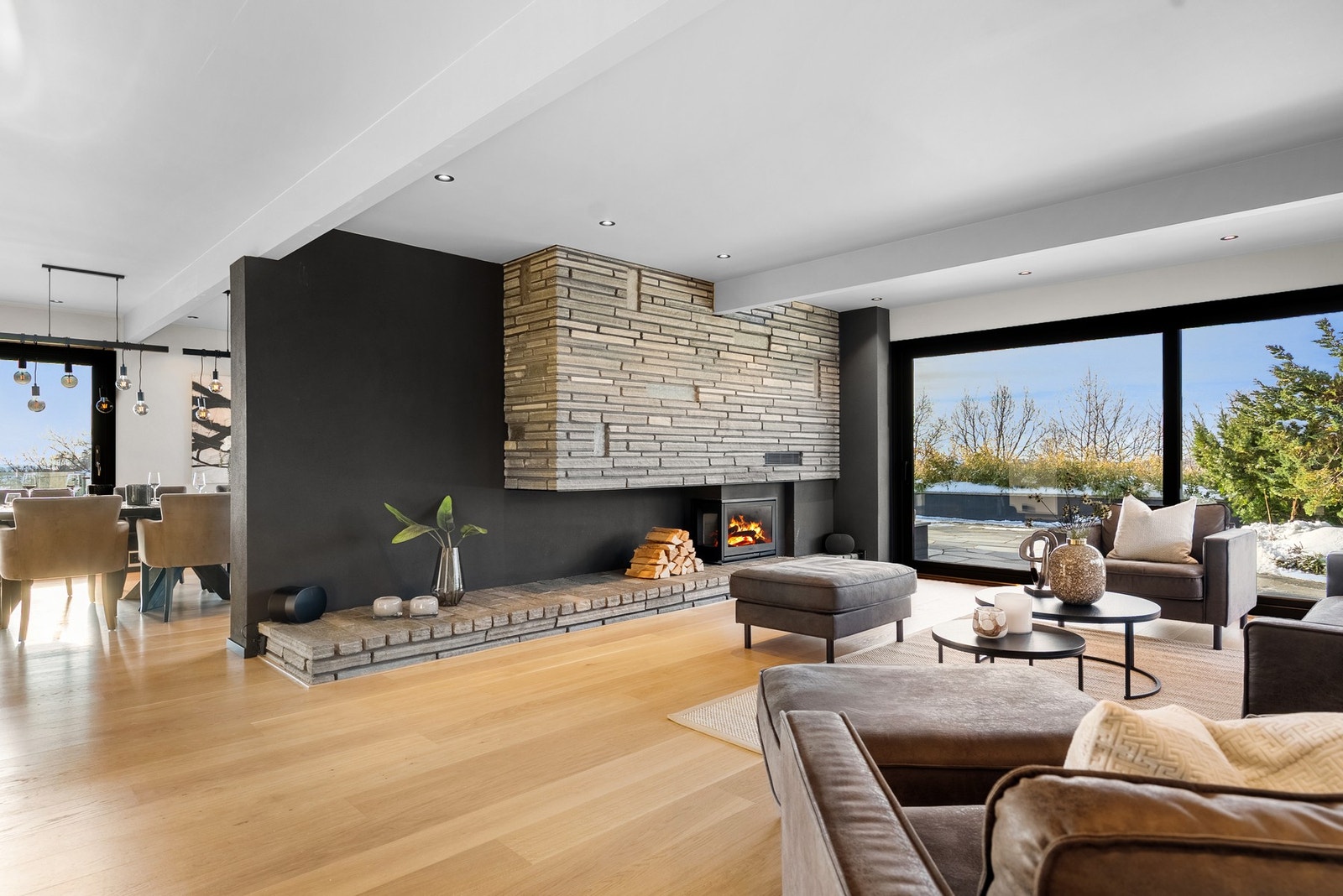 I stuen får du en harmonisk kombinasjon av slette, moderne flater og en peisovn som står i naturlig stil med terrenget utenfor og skaper en lun og helhetlig atmosfære Galleribilde