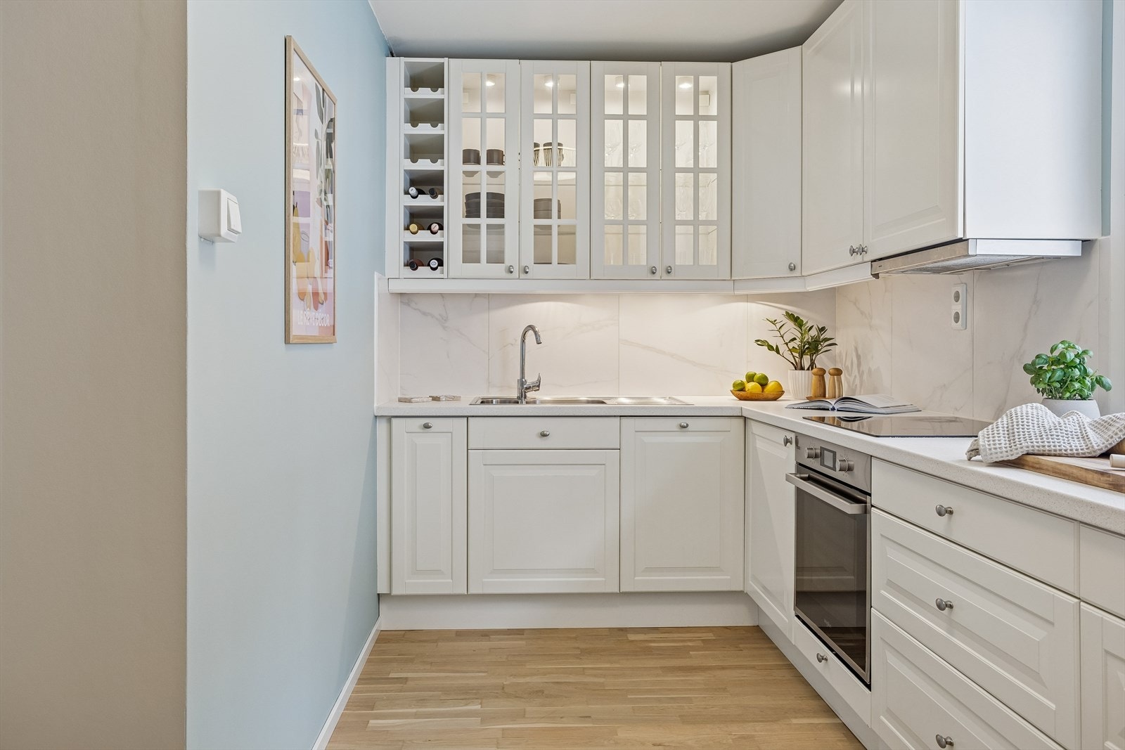 Kjøkkenet har en tidløs innredning med profilerte fronter, vitrineskap og integrerte hvitevarer. Fliser over benken forenkler renholdet. Galleribilde