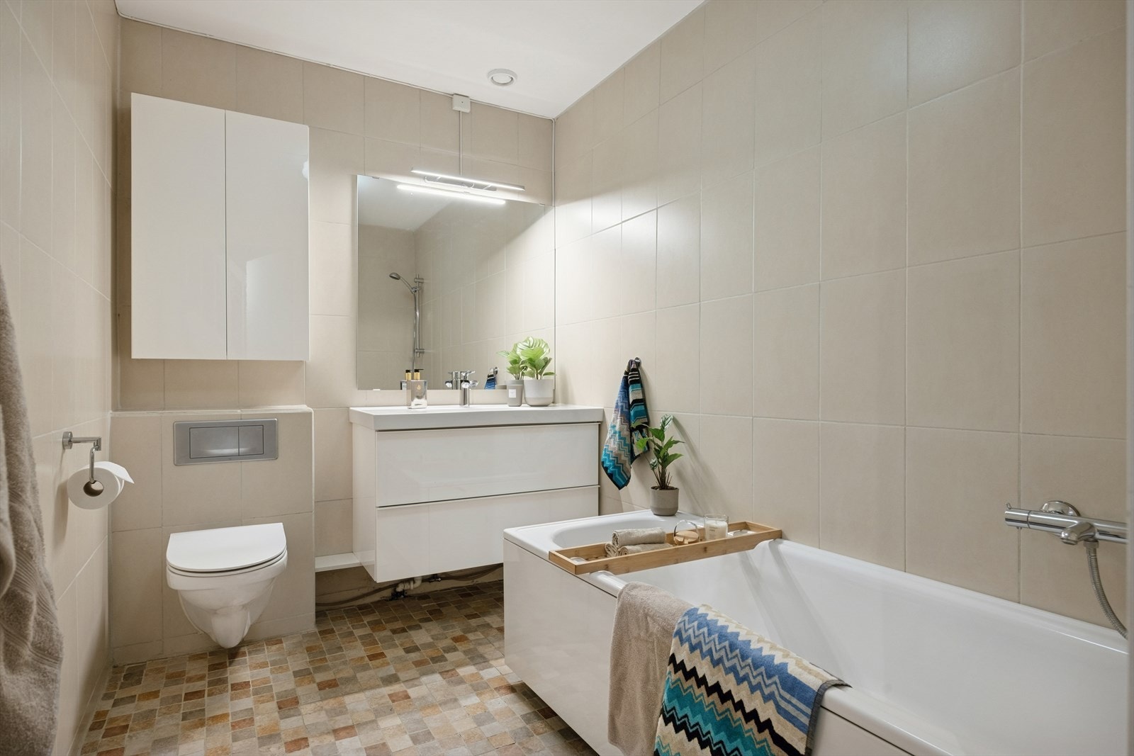 Hovedbad utstyrt med badekar med dusjgarnityr på vegg, vegghengt toalett og innredning med servant. Galleribilde