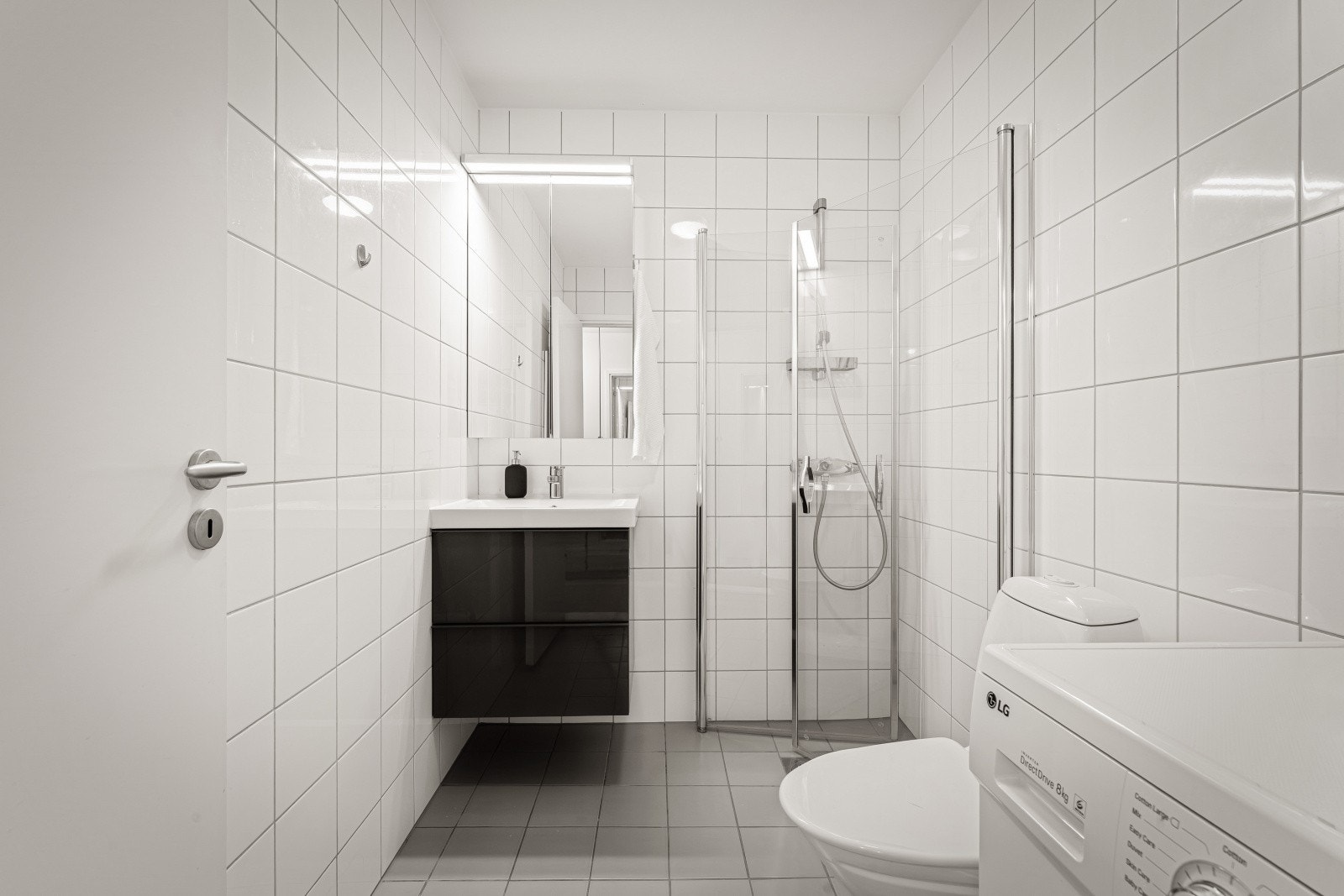 Tidløs innredning bestående av foldedører i dusj, toalett og baderomsinnredning med heldekkende servant, samt belyst speil. Galleribilde