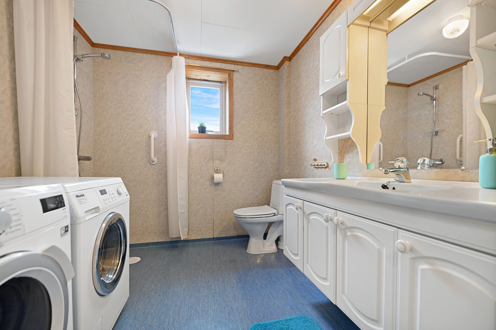 Baderom med dusj, toalett, vaskemaskin og servant. Vinduer gir naturlig lysinnslipp. Galleribilde