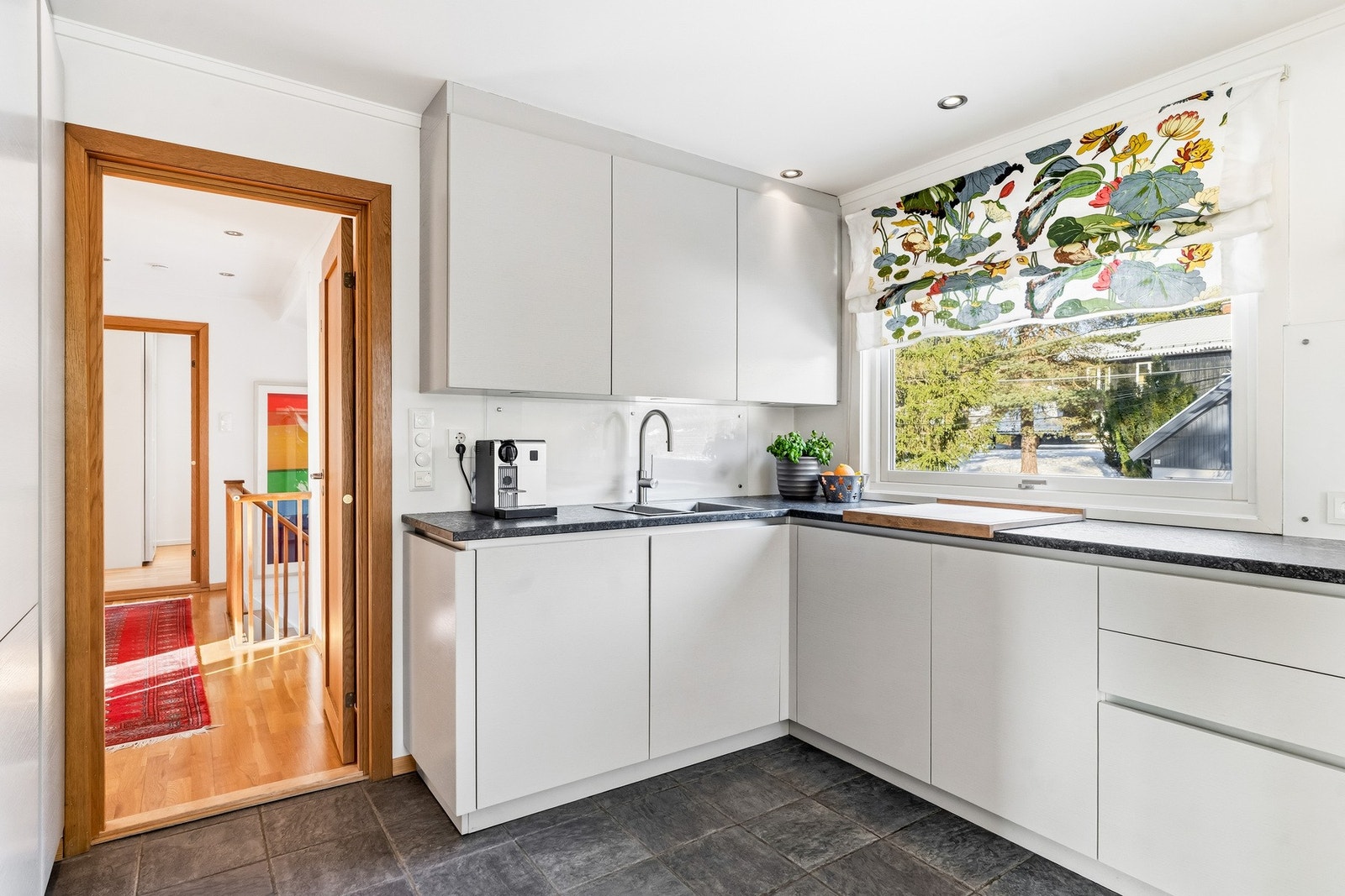 Benkeplaten er i granitt med underlimt metallvask fra Blanco og ettgreps kjøkkenarmatur, og det er montert glassplate som sprutbeskyttelse mellom benkeplate og overskap samt over stekesonen. Galleribilde