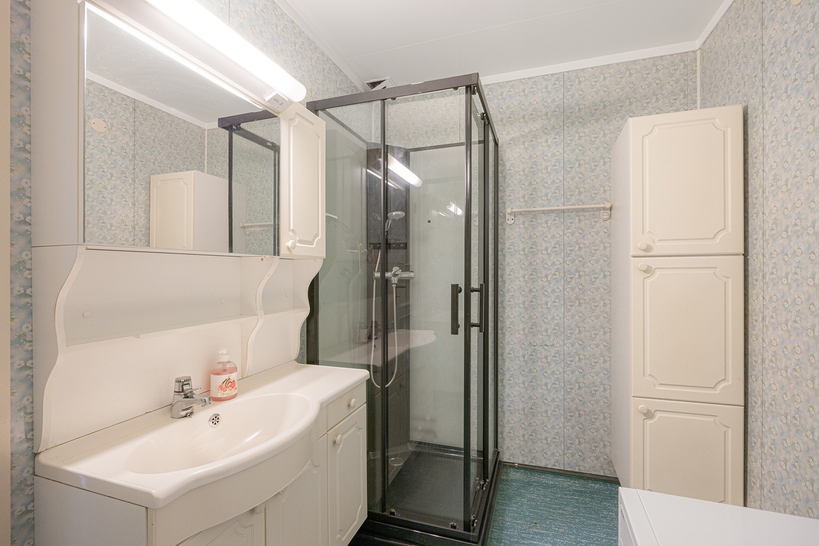 Baderomsinnredningen med heldekkende servant, speilskap med belysning, dusjkabinett og opplegg for vaskemaskin. Galleribilde