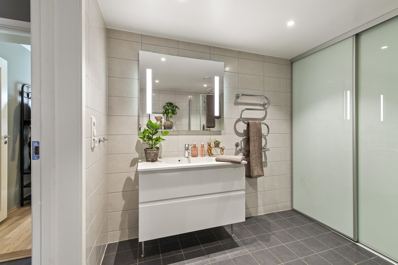 Badet fremstår stilrent og helfliset, og er utstyrt med innfellbare dusjvegger, toalett og baderomsinnredning med servant. Galleribilde