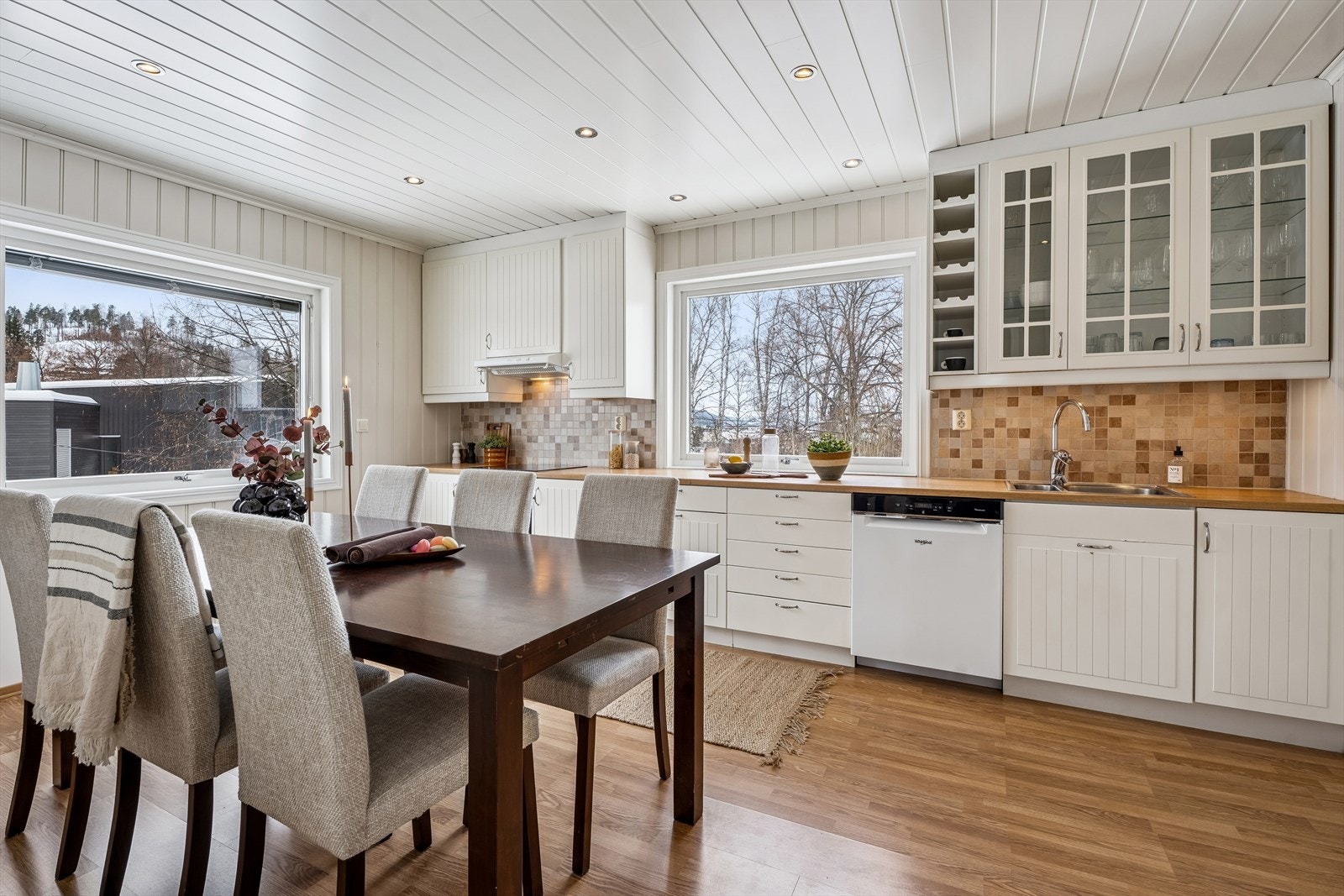 Takhøy kjøkkeninnredning i klassisk stil, fliser over benk og godt med dagslys inn fra to sider. Galleribilde