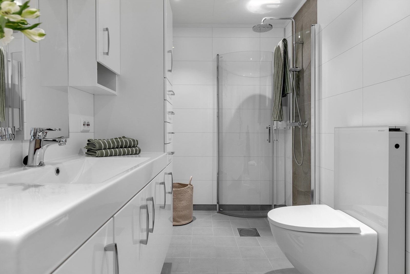 Baderom med flislagt gulv med gulvvarme, dusjvegger, vegghengt toalett og romslige innredninger. Galleribilde