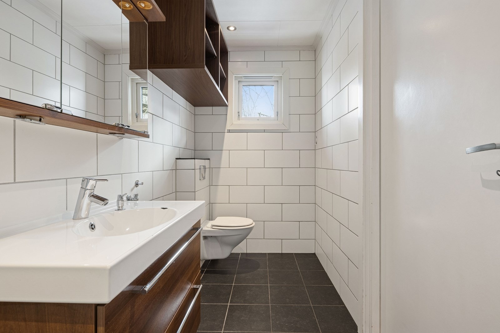 Pent flislagt bad med toalett, opplegg for vaskemaskin, dusjhjørne og servant med speil. Galleribilde