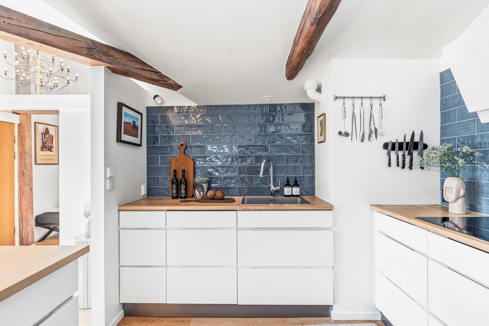 Topplimt metallvask og kjøkkenarmatur med spylefunksjon. Over benkeplaten er det fliser på veggen, induksjonstopp og avtrekksvifte ble montert i 2021. Galleribilde