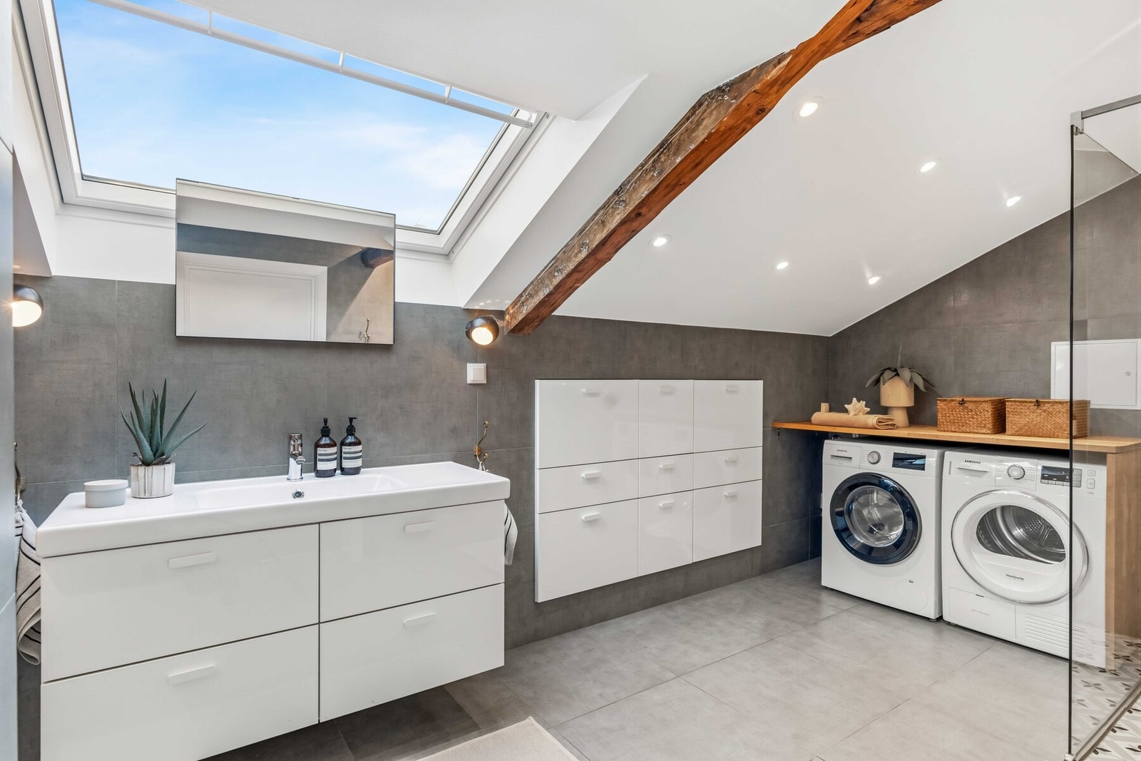 Romslig og helfliset bad med skrå himling, takvindu, downlights, veggmontert toalett og opplegg for vaskemaskin og tørketrommel under heltre benkeplate. Galleribilde
