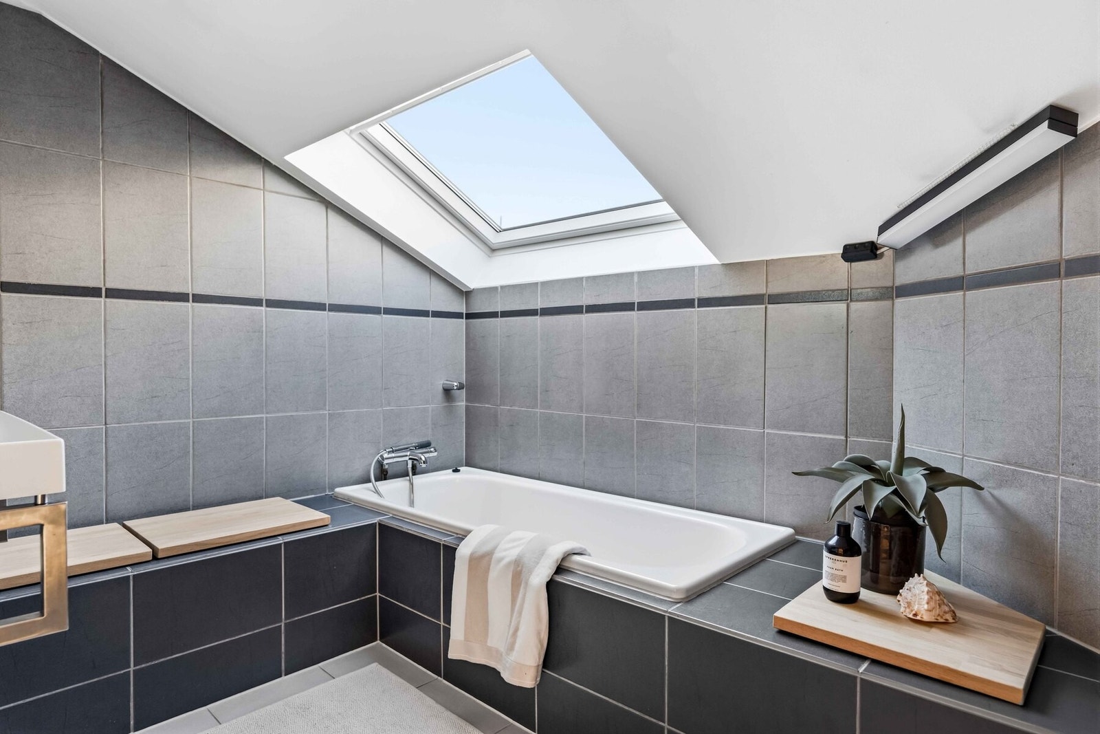 Et romslig, flislagt bad 2. Belysningen består av vegglamper, samt takmontert lampe. På gulvet er det fliser i format 30 x 30 cm med varmekabler. Innredningen består av veggmontert servantskap og innfliset speil. Videre har rommet veggmontert toalett og Galleribilde