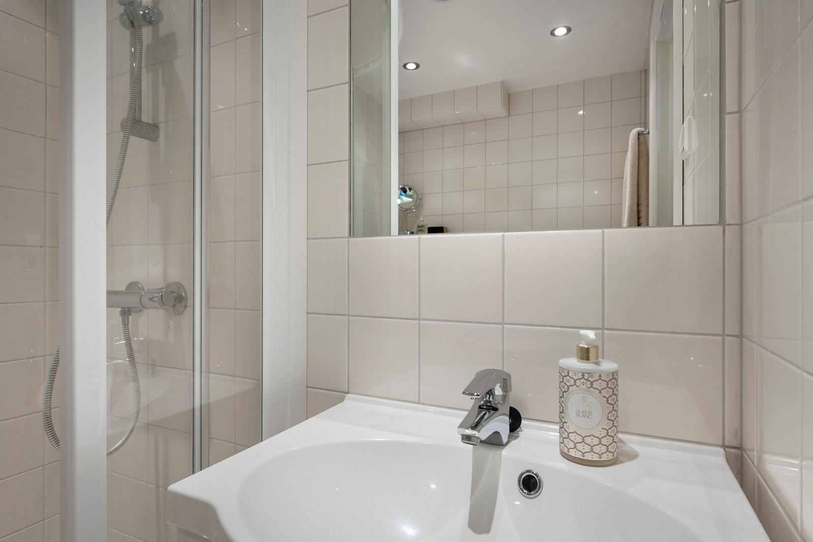 Dusjhjørne med dører og vegghengt dusjarmatur. Vegghengt toalett og mekanisk avtrekk med ventil i himling. Galleribilde