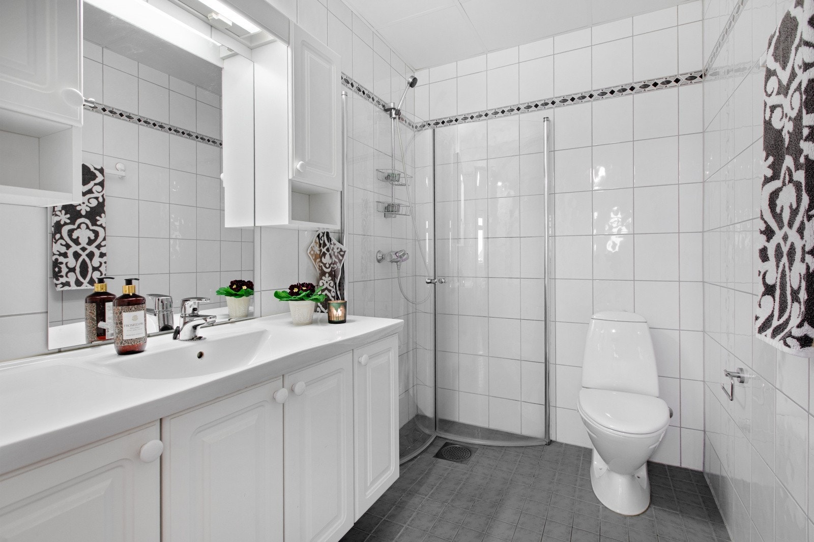 Badet har en praktisk dusjnisje med innfellbare glassdører, samt toalett og servantinnredning med speil. Galleribilde