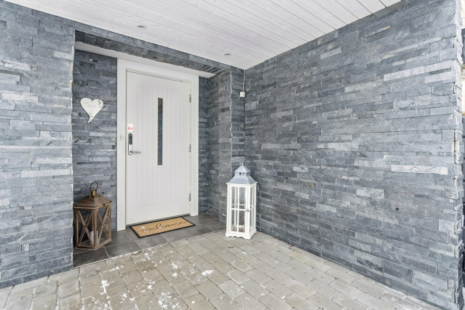 Overbygget inngangsparti med utvendig steinpanel og belegningsstein på gårdsplassen. Galleribilde