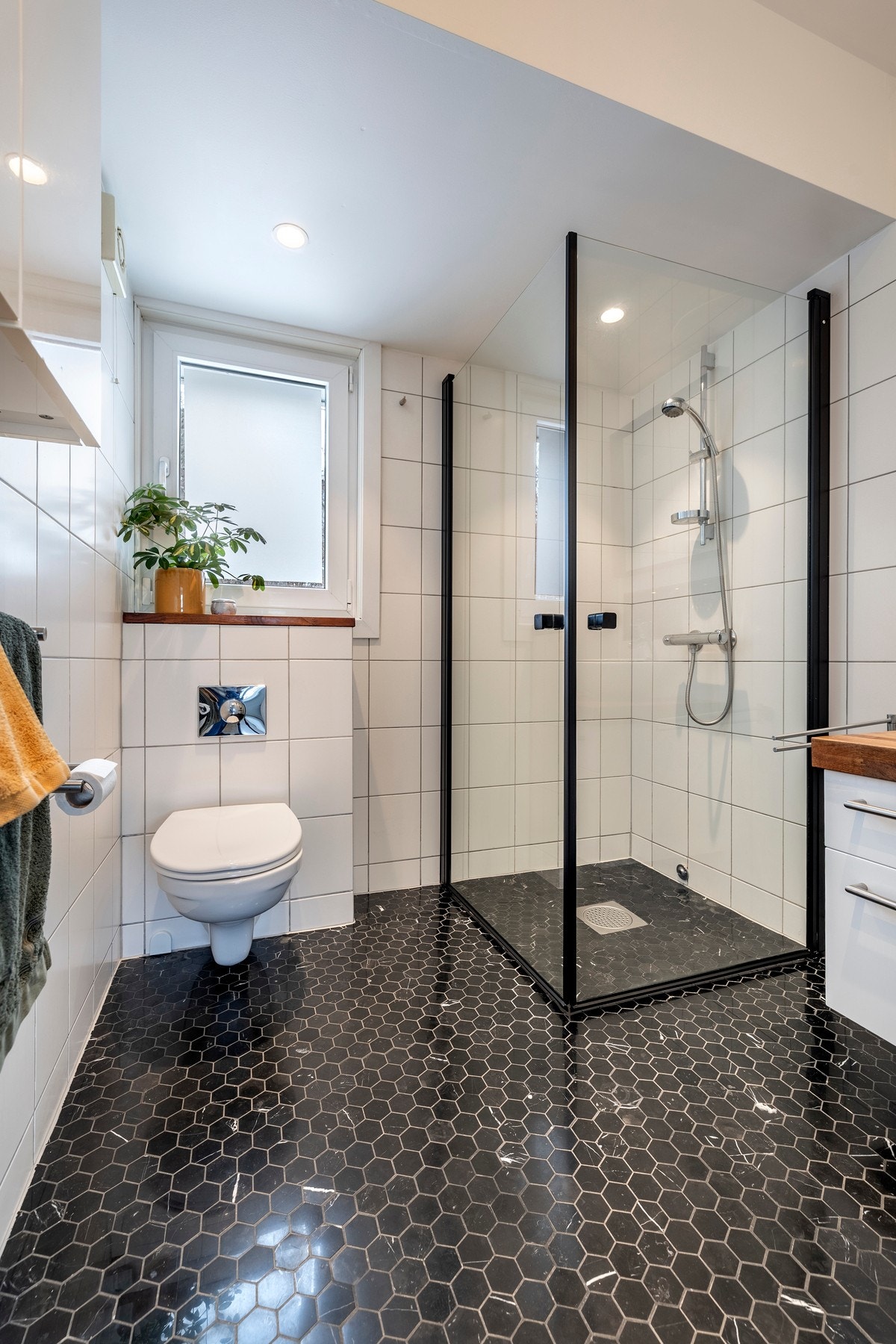 Innredet med servantinnredning med bollevask, speil over servant, veggskap, vegghengt toalett og dusjhjørne med svingbare glassdører. Galleribilde