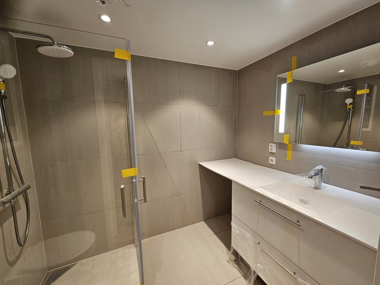 Moderne flislagt bad (60x60) med dusjhjørne, romslig innredning med skuffer, speil med lys og opplegg til vaskemaskin. Det gjøres oppmerksom på at benkeplate blir byttet til en tykkere og mer solid plate. Galleribilde