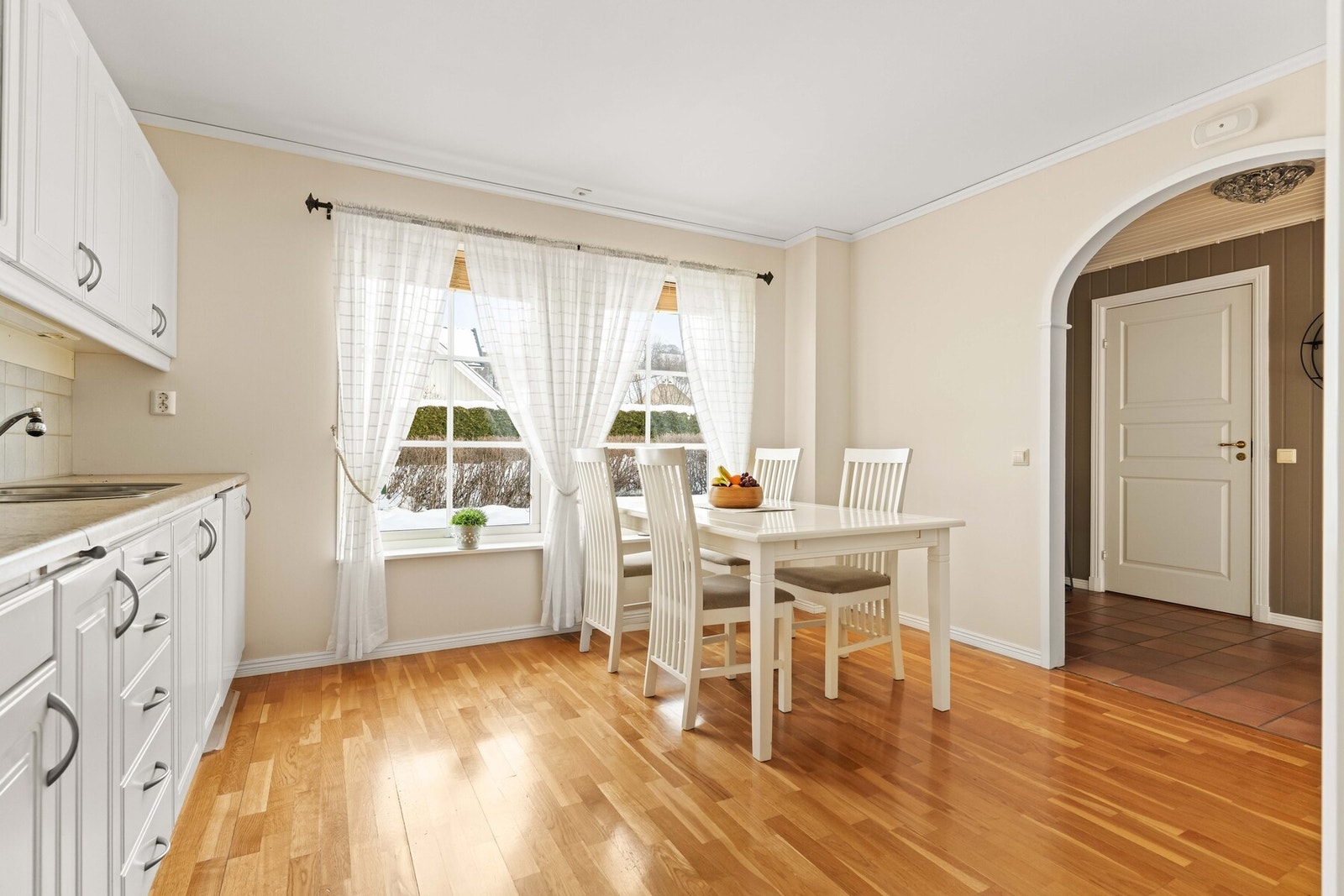 Spiseplassen er trukket mot vinduet og får en naturlig ramme av det myke dagslyset som slipper inn gjennom de lette gardinene. Galleribilde