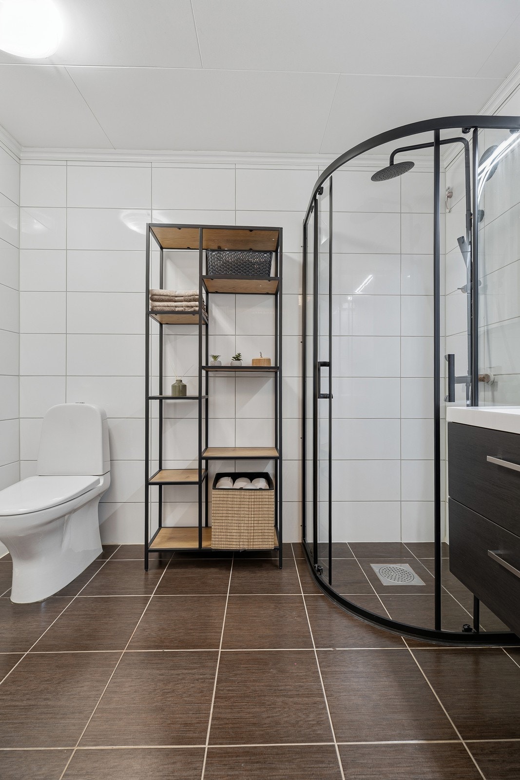 Badet er innredet med dusjsone, toalett og heldekkende servant i baderomsinnredning Galleribilde