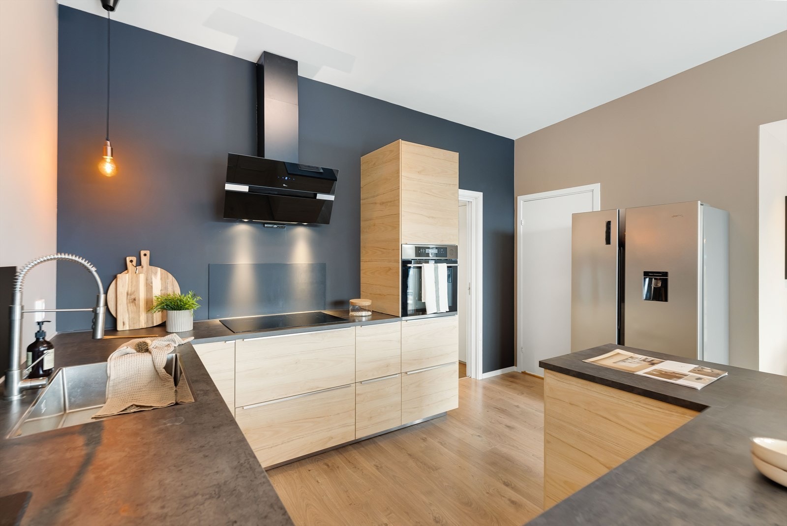 Benkeplate med nedfelt vask og platetopp. Innredningen innehar steikeovn, oppvaskemaskin og frittstående kjøle,- og fryseskap Galleribilde