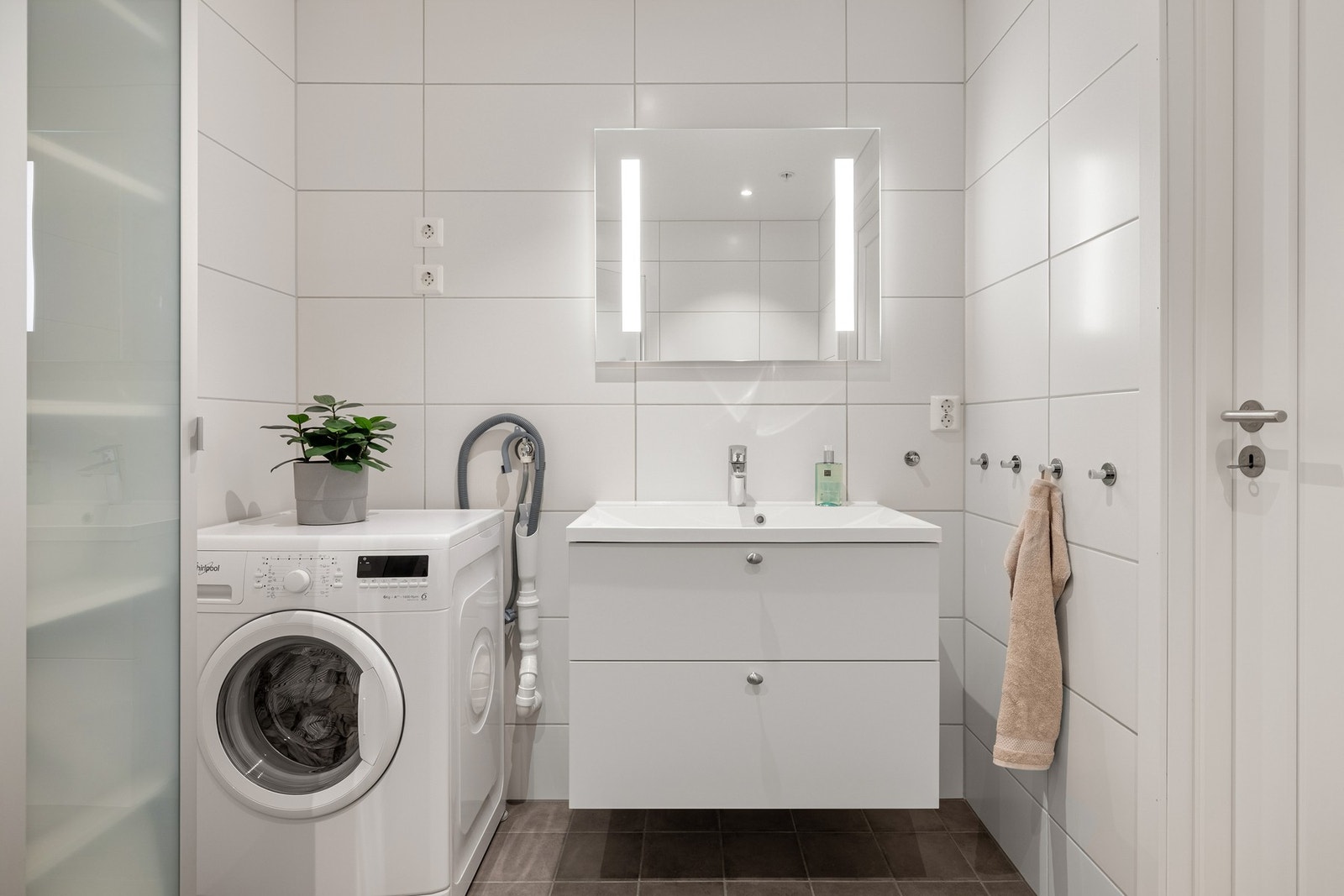 Badet er innredet med dusj med glassvegger, vegghengt toalett, baderomsinnredning og opplegg for vaskemaskin. Galleribilde