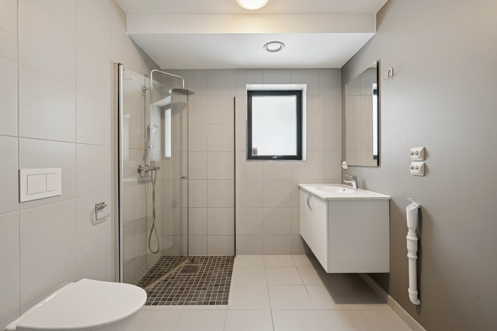 Flislagt bad med varmekabler, dusj, vegghengt toalett og opplegg for vaskemaskin. Galleribilde