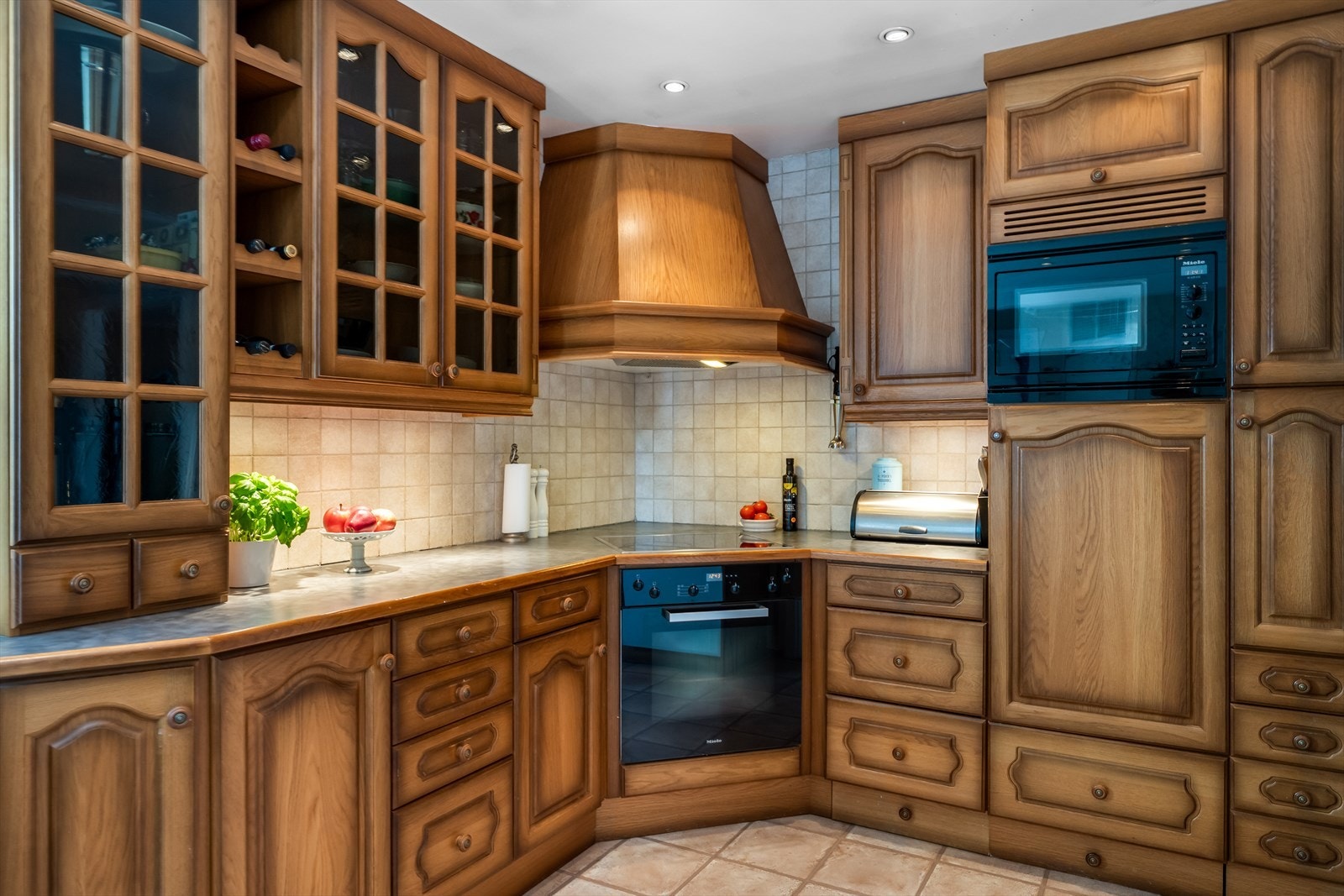 Kjøkkeninnredning 1. etg. med profilerte fronter og laminert benkeplate med fliser på vegg over benkeplaten. Hvitevarer: kjøleskap/fryser, kjølehjørne, oppvaskmaskin, platetopp, ovn og micro. Det er kjøkkenventilator med avtrekk ut. Galleribilde