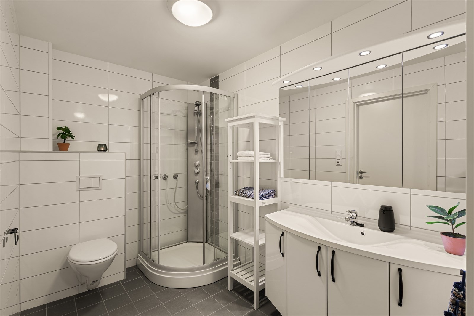 Badet er av god størrelse og inneholder servant med innredning og speil, belysning, vegghengt toalett, dusjkabinett samt opplegg for vaskemaskin Galleribilde