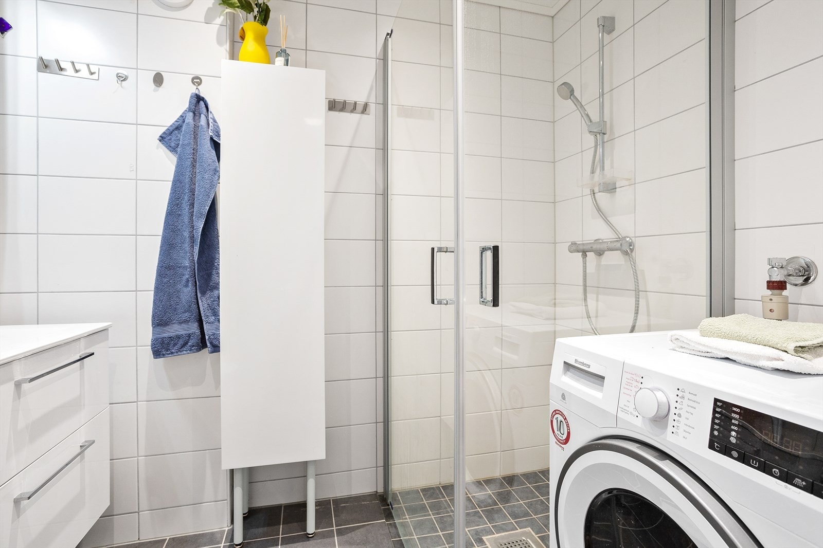 Badet er innredet med nedfelt servant, veggmontert toalett, dusjhjørne med glassvegger og opplegg for vaskemaskin. Galleribilde