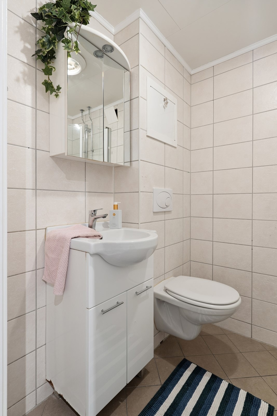 Rommet har innredning med nedfelt servant, overskap med speil, veggmontert toalett, dusjhjørne med innfellbare dusjdører og opplegg for vaskemaskin. Galleribilde