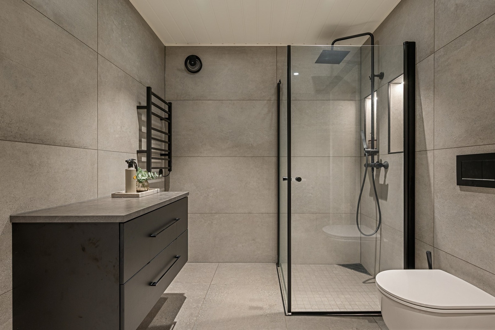 Flislagt bad med moderne innredning, dusjvegger og vegghengt toalett. Galleribilde