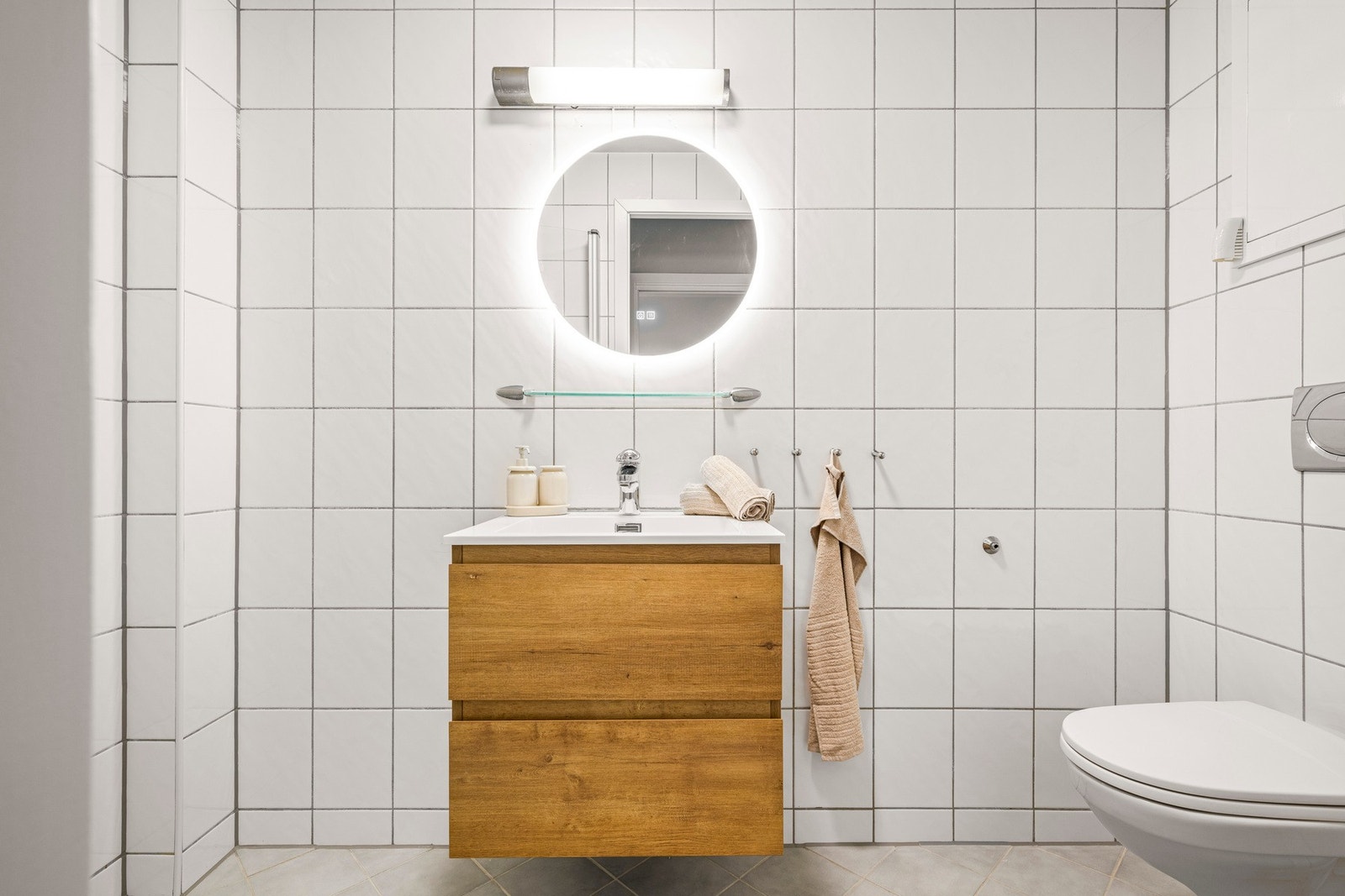 Badet inneholder vegghengt toalett, helstøpt servant, skap under servant med slette fronter, dusjdører i klart glass og opplegg for vaskemaskin. Galleribilde