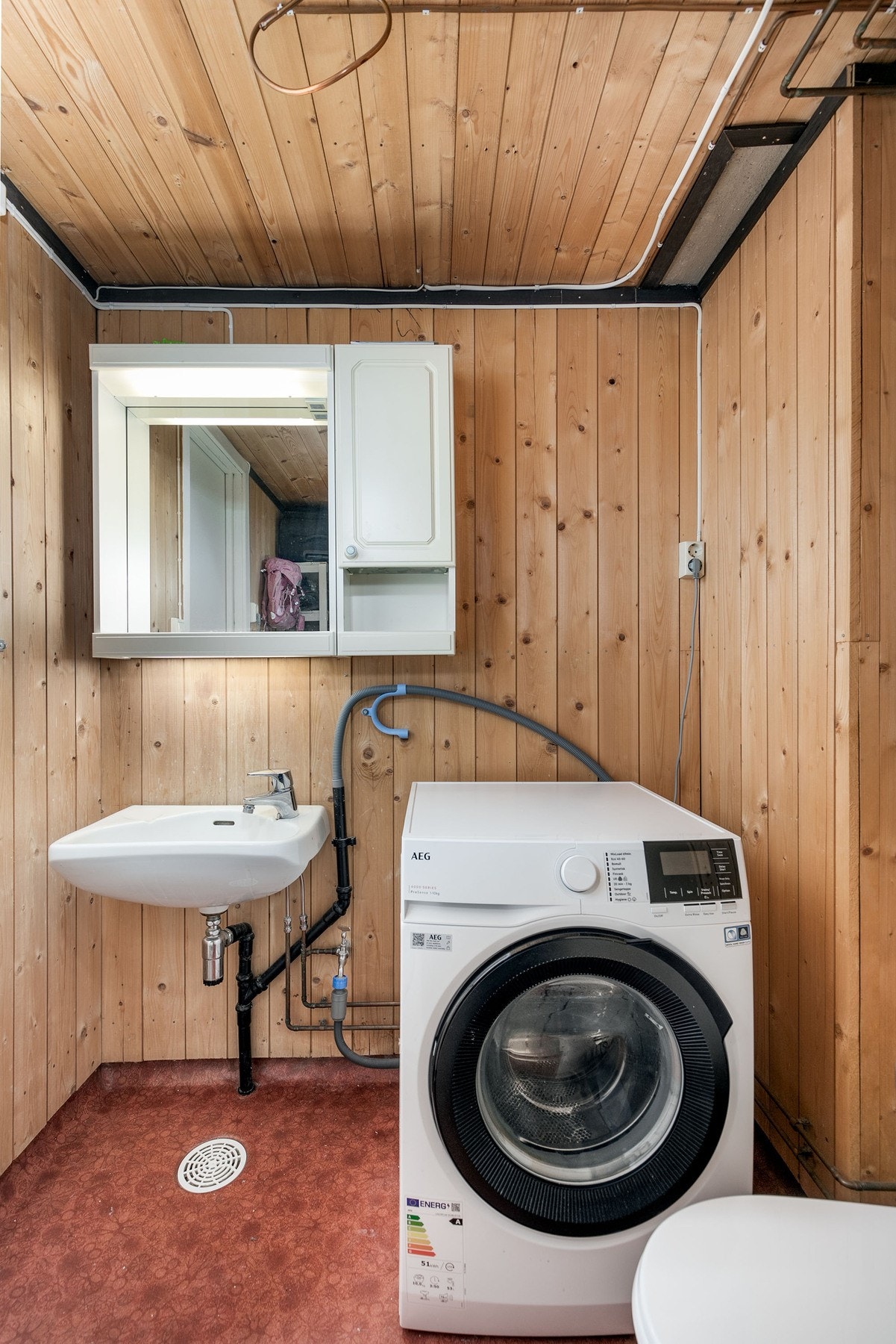 Vaskerom med trepanel på vegger og tak, samt en vaskemaskin og servant. Galleribilde