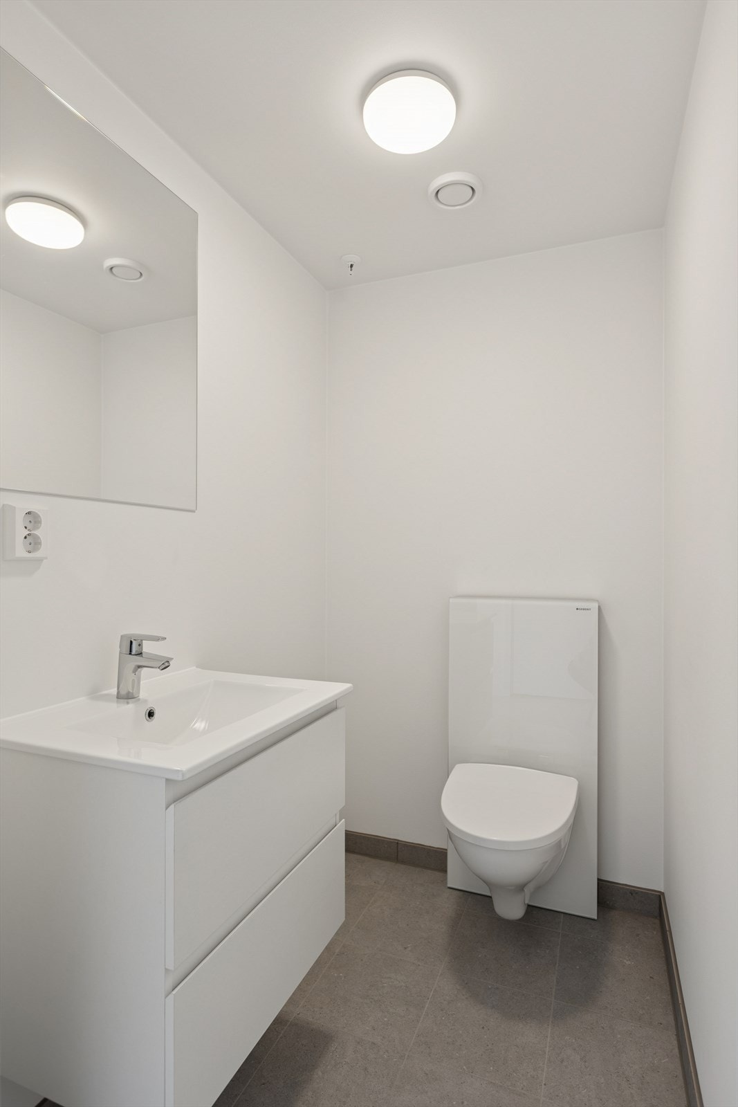 Separat wc/toalettrom med flislagt gulv, malte vegger og downlights i himling. Rommet er utstyrt med servant med fabrikklakkerte fronter, speil på vegg over servanten, samt veggmontert toalett. Galleribilde