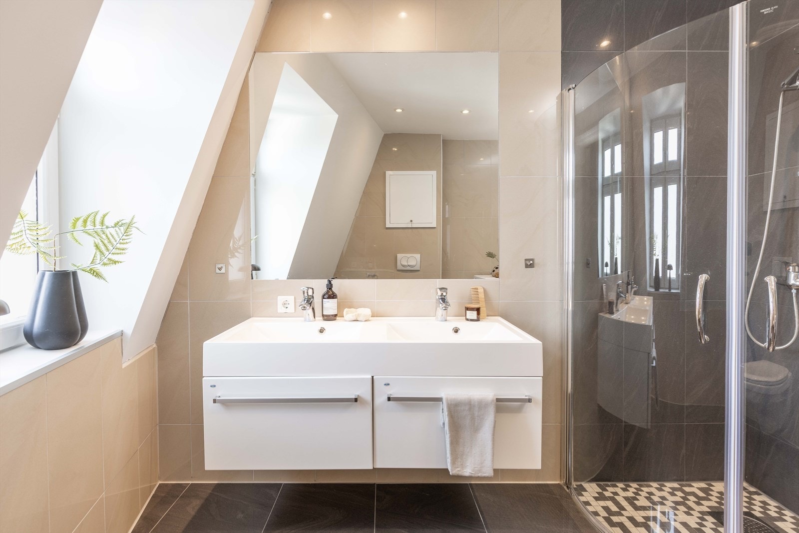 Badet er innredet med baderomsmøbel med slette fronter og dobbel heldekkende servant med speil over. I tillegg er det innredet med dusj med foldedører i herdet glass og vegghengt toalett. Galleribilde