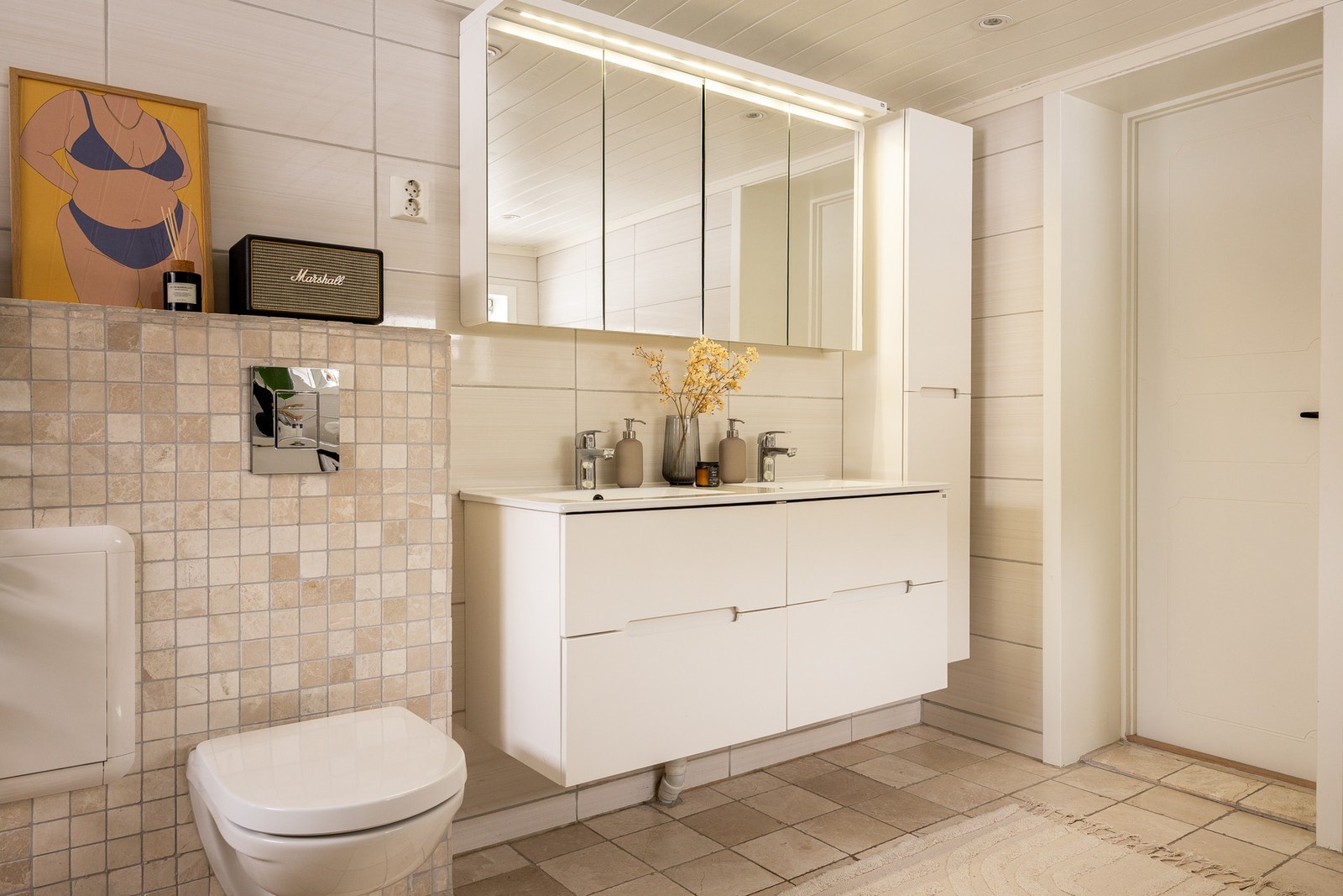 Badet er innredet med dusjnisje med innfellbare dusjdører, badekar, dobbel servant med ettgreps blandebatterier og vegghengt toalett. Galleribilde