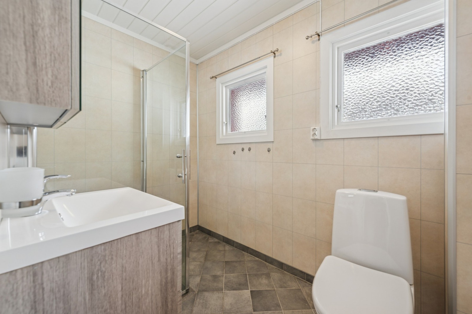 Lyst og tiltalende baderom med moderne dusjløsning, pen servantinnredning og toalett. Badet tilbyr flislagt gulv med gulvvarme og vegger kledd med baderomsplater, som skaper et tidløst uttrykk. Galleribilde