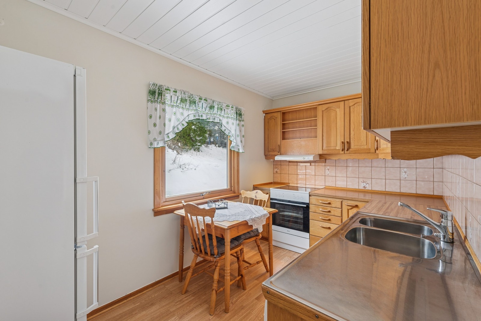 Det er også plass til en mindre spisegruppe ved vinduet, perfekt for frokost eller en rolig kaffestund. Ventilator, oppvaskmaskin og hvitevarer egner seg godt til kjøkkenets enkle og funksjonelle stil. Galleribilde