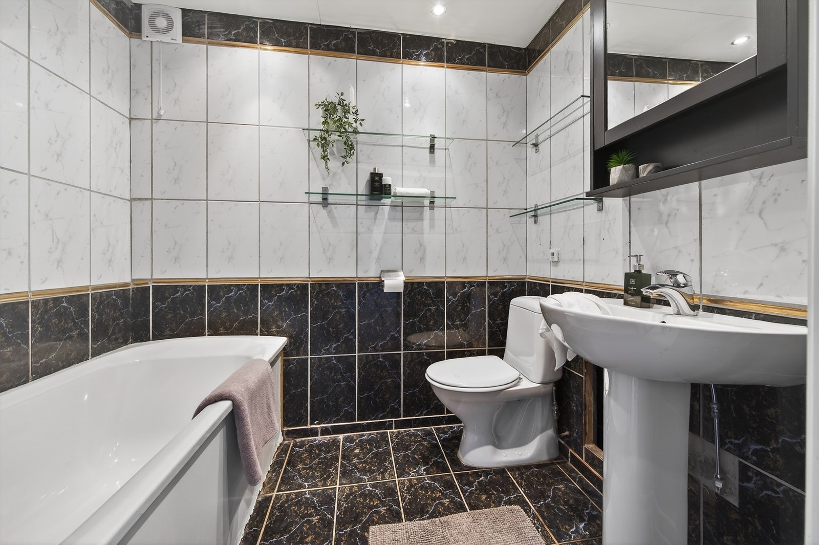 Flislagt baderom bestående av porselensvask på piedestal, toalett og badekar Galleribilde