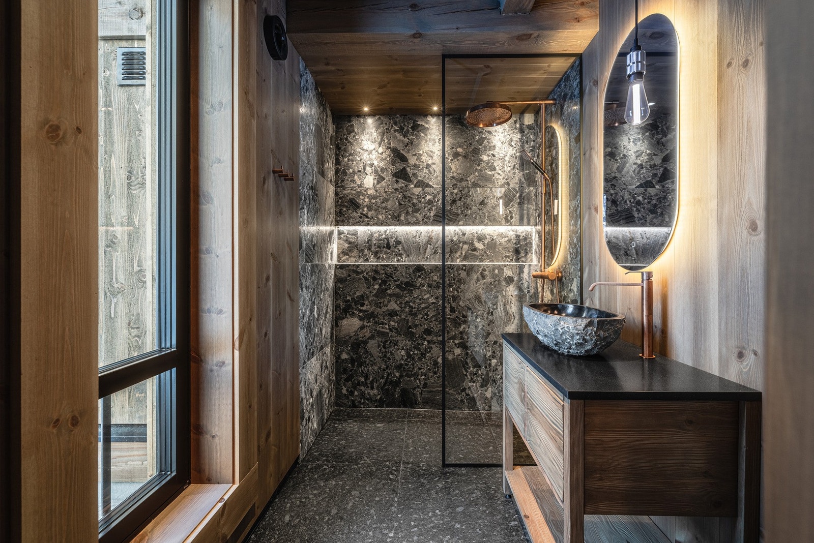 Elegant baderom med steinvask og varme naturmaterialer som skaper en lun og spa-inspirert atmosfære. Galleribilde