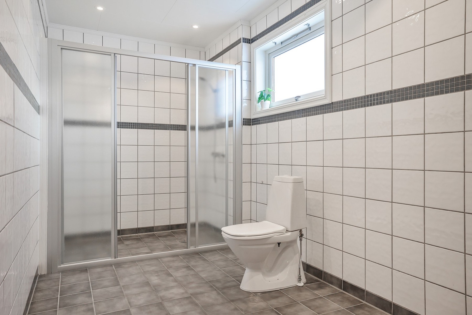 Baderommet inneholder dusjnisje med glassvegg og glassdør, og gulvstående toalett. Galleribilde