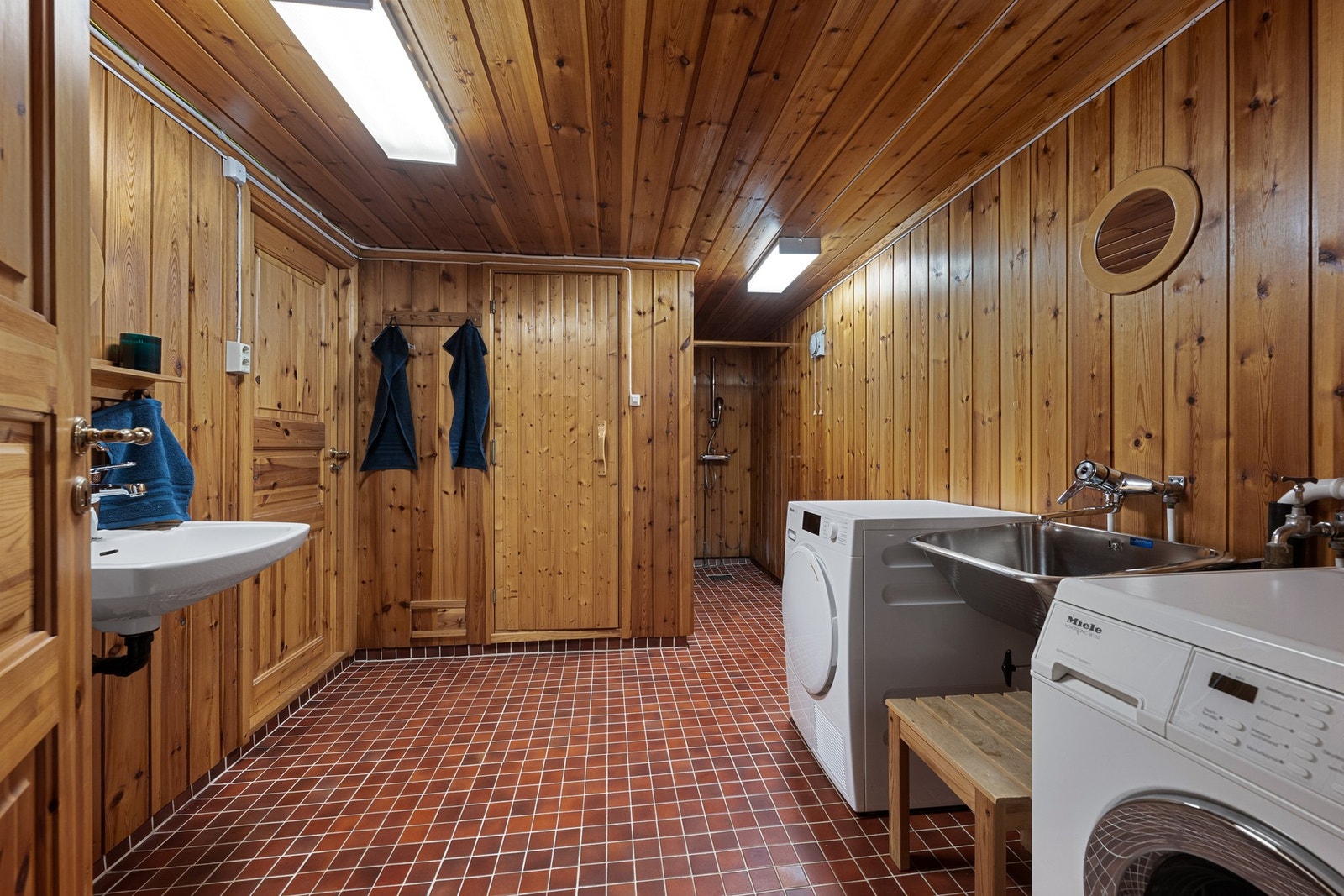 Romslig vaskerom/bad med god arbeidsplass, skyllekum i stål og opplegg for vaskemaskin og tørketrommel. Galleribilde