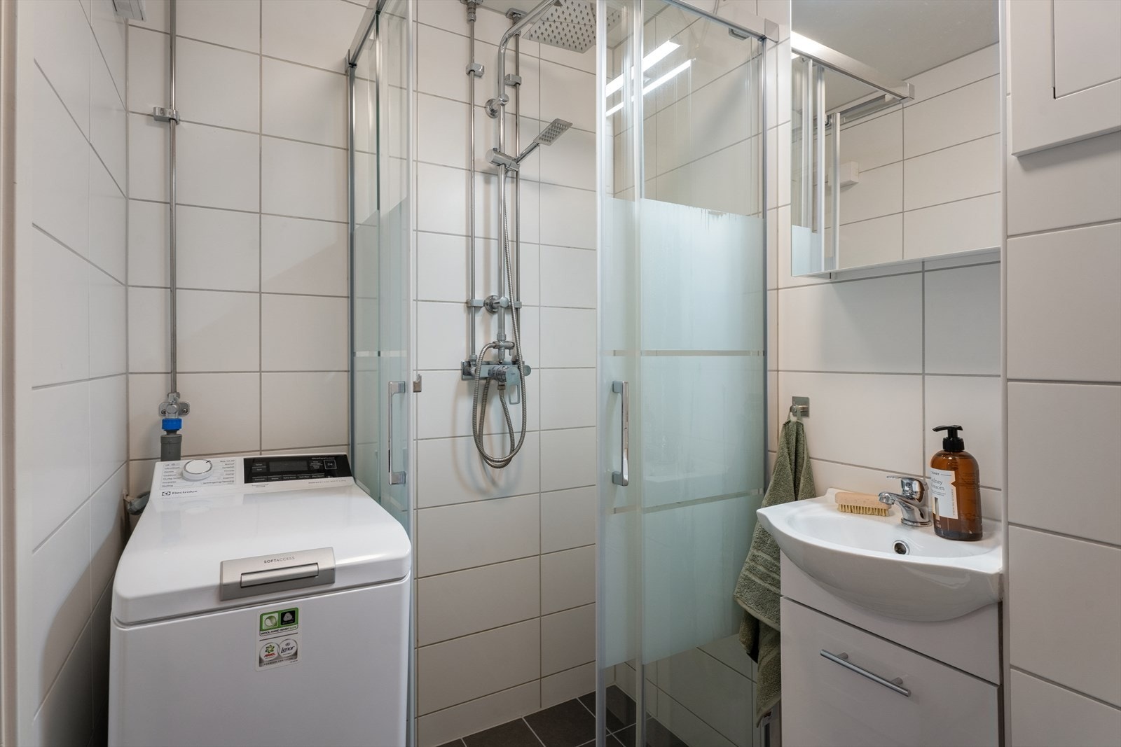 Pent og flislagt bad rehabilitert i 2024, med praktisk dusjhjørne, nedfelt servant, veggmontert toalett og speilskap med belysning. Galleribilde