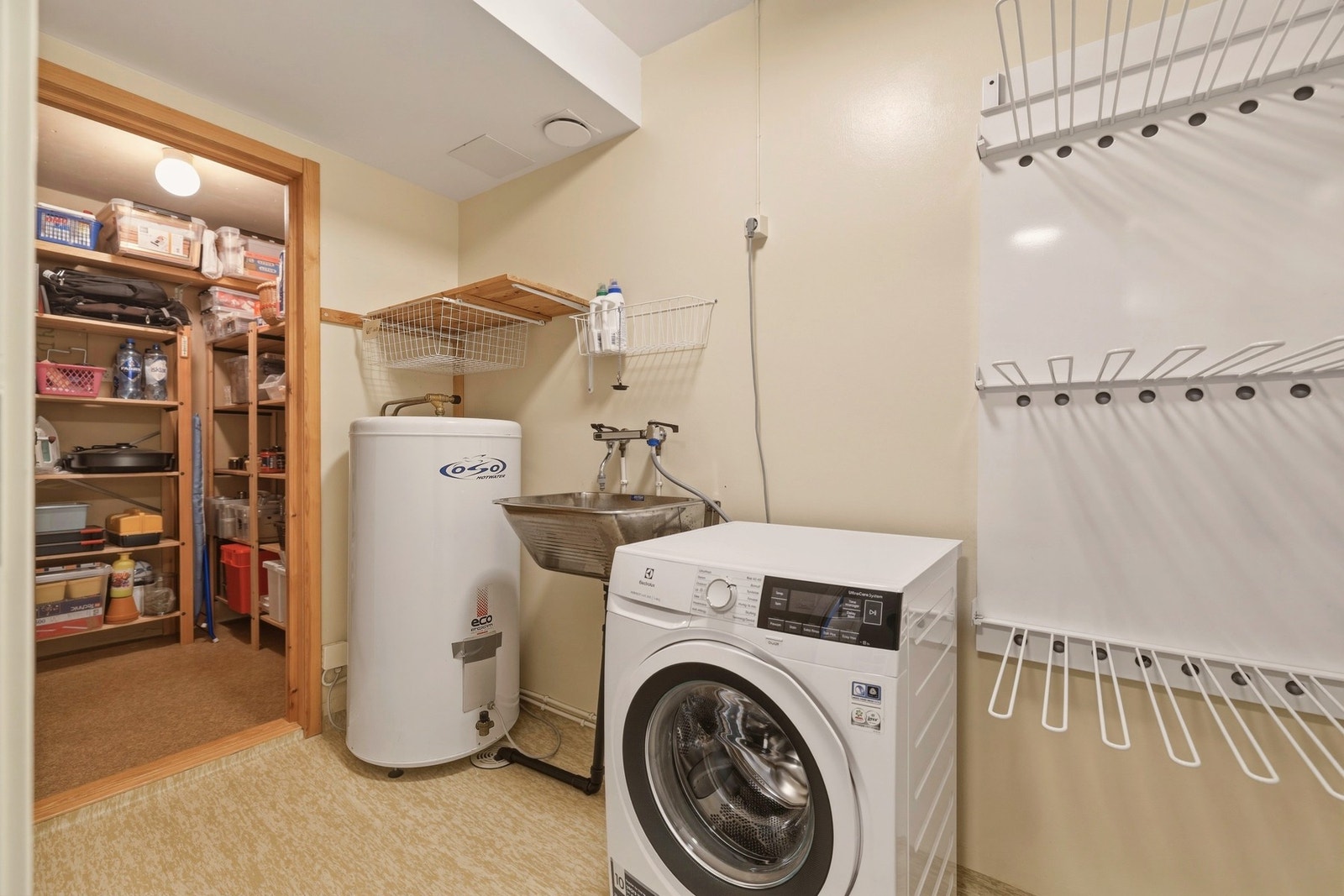 Praktisk vaskerom med utslagsvask, varmtvannstank og opplegg for vaskemaskin. Rommet har oppgraderingsbehov. Inngang til bod for gode lagringsmuligheter. Galleribilde
