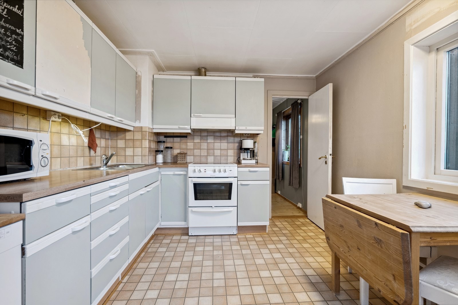 Vinklet innredning med laminat benkeplate med nedfelt oppvaskbenk beslag. Slette kremfargede fronter. Galleribilde