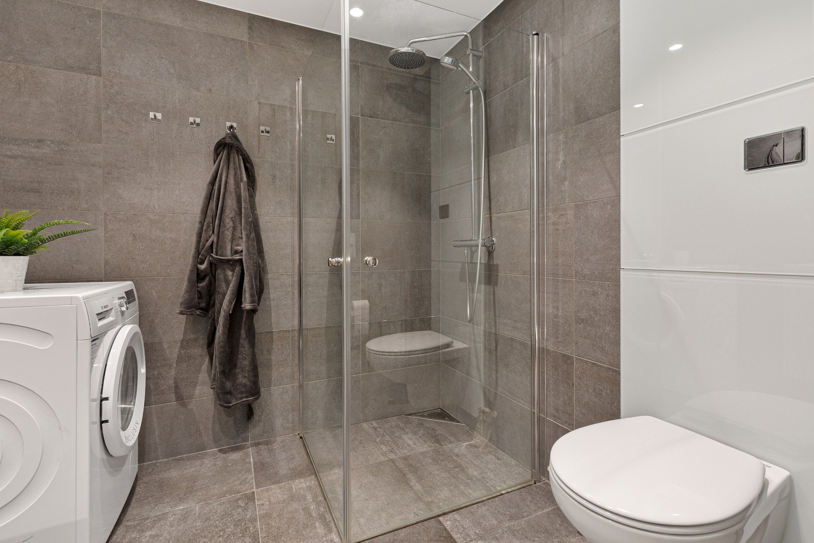 Badet har moderne grå fliser på gulv og vegger. Dusjhjørne med innfellbare glassdører. Galleribilde