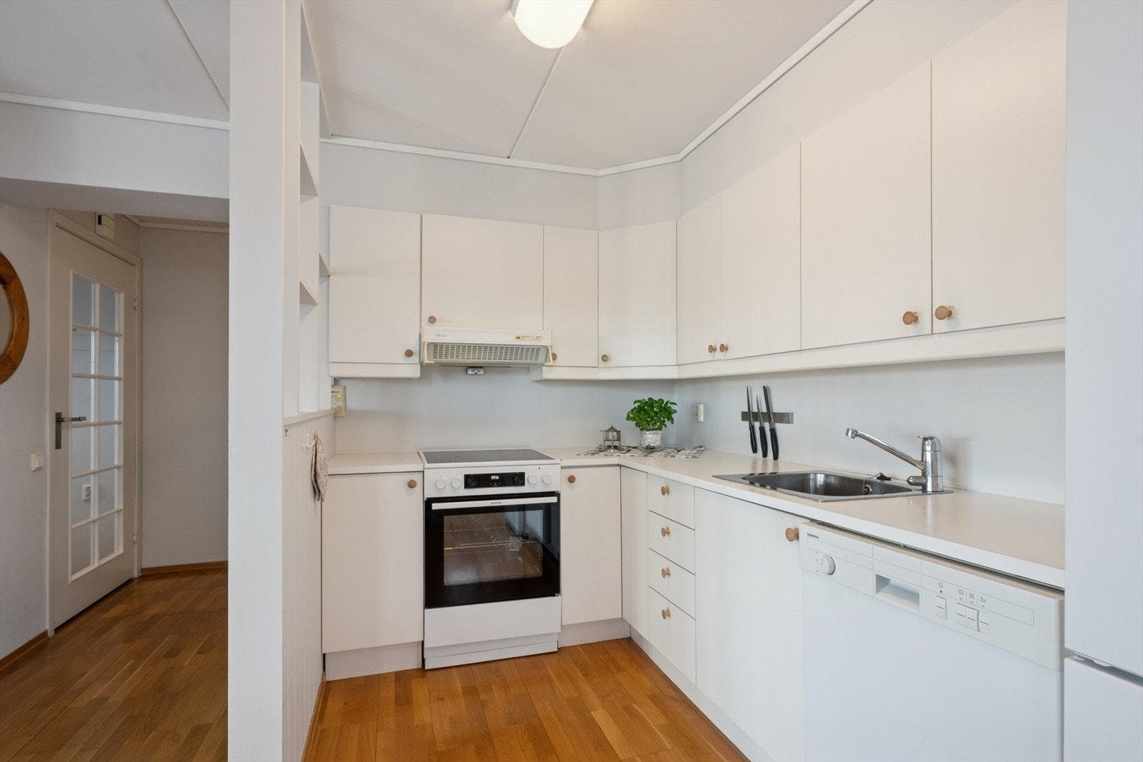 Kjøkkenet har en pen innredning med hvite, glatte fronter og hvit laminert benkeplate med nedfelt oppvaskkum i rustfritt stål. Galleribilde