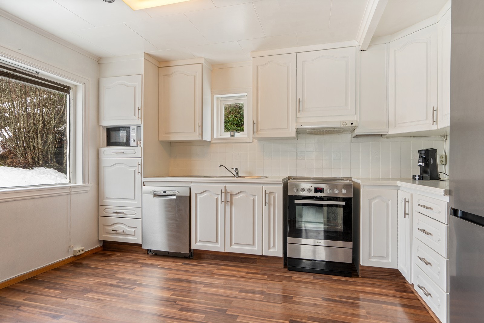 Kjøkkenet består av profilerte fronter i hvit utførelse og benkeplate av laminat med nedfelt vask. Galleribilde